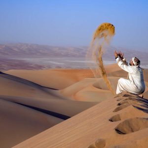 Man in traditional outfit in a desert at sunrise, throwing sand