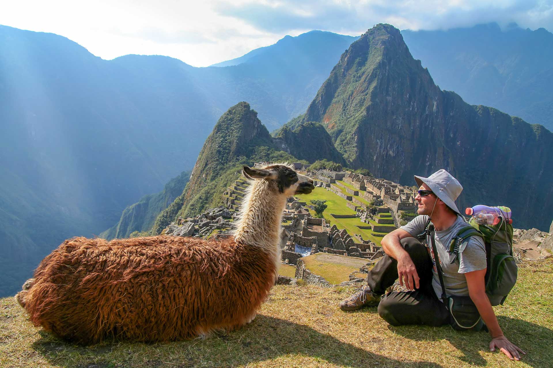 Tourist and llama sitting in front of Machu Picchu, Peru